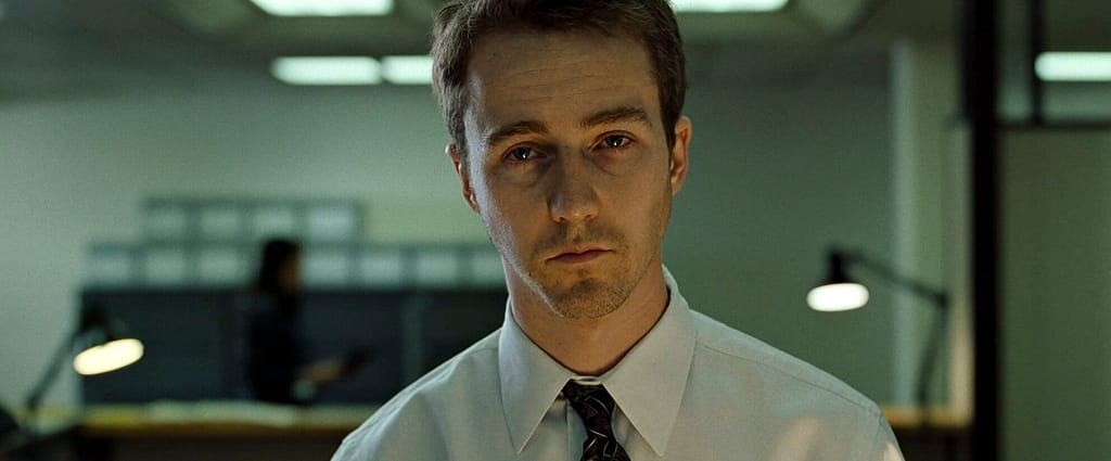 Fight Club protagonist staring blankly in a sterile office, representing emotional numbness and psychological dissociation caused by modern life.