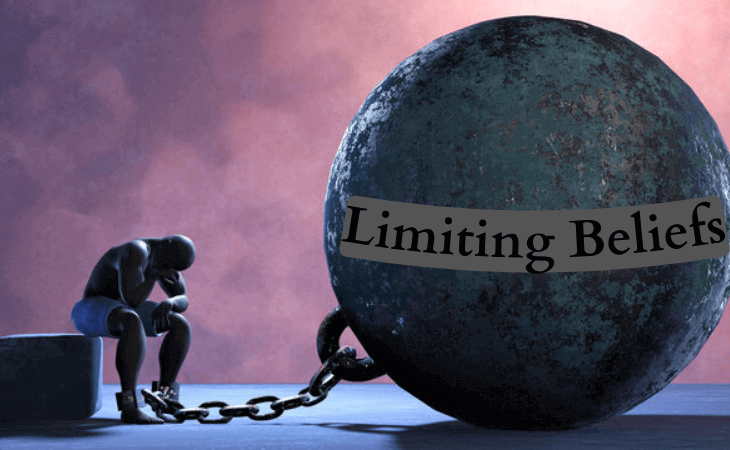 Person chained to a giant ball labeled “Limiting Beliefs,” symbolizing psychological barriers to growth.