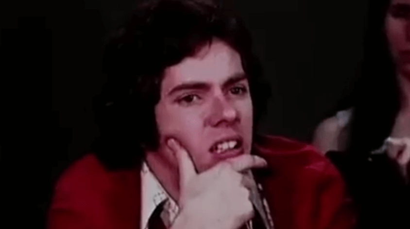 Man in red sweater grimacing in confusion during a group conformity test