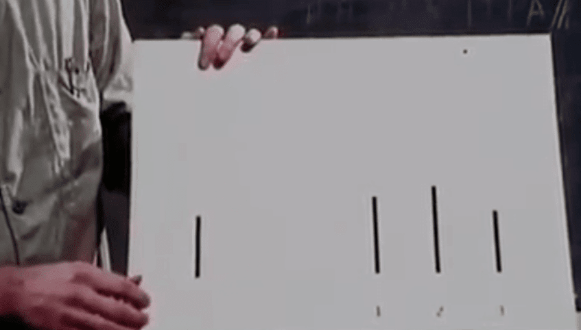 Hand holding a board with four vertical lines used in a visual conformity test